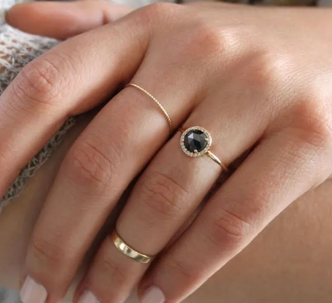 A round-cut black diamond ring encircled by a halo of diamonds with a sleek gold band.
