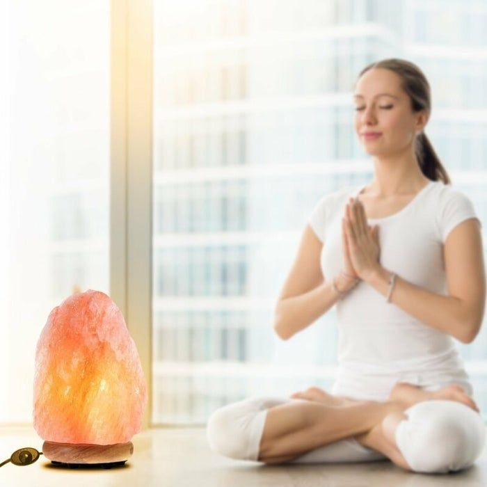 A glowing salt lamp beside a woman in a meditative pose