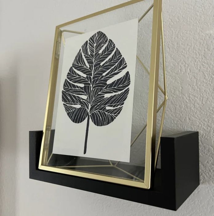 A reviewer's snapshot of a gold leaf-patterned frame elegantly displayed on a black wall shelf