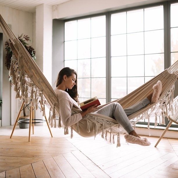 Model reading a book while lounging on a fringed hammock