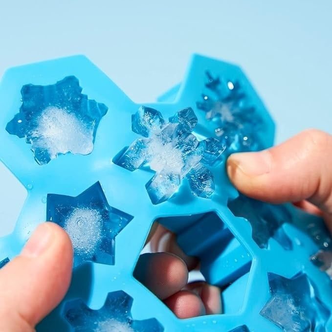 A person removing a snowflake-shaped ice cube from a silicone mold