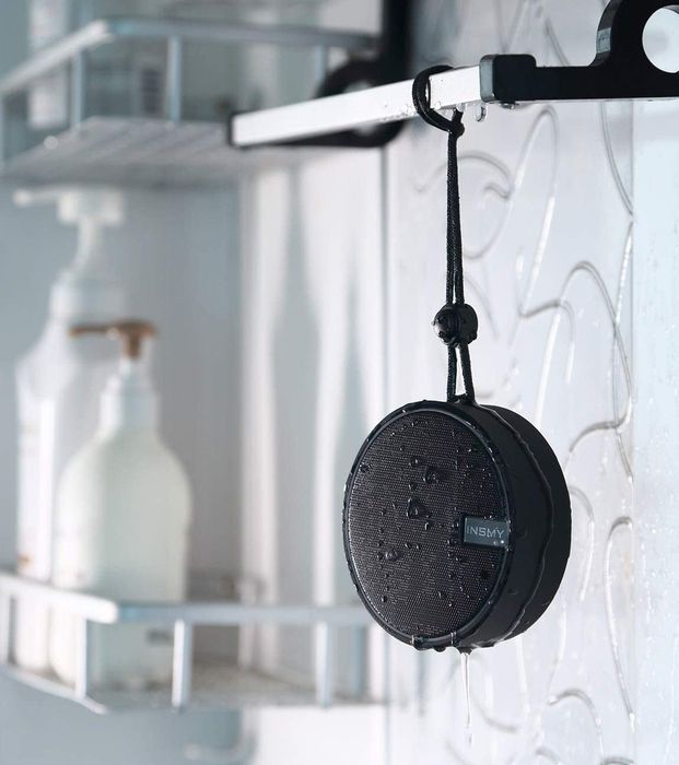 A wet INSMY Bluetooth speaker hanging from a bathroom shelf.
