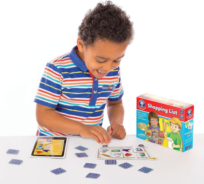 A child enthusiastically plays the Shopping List board game at a table. The game box, adorned with illustrations of two animated characters, is also visible.