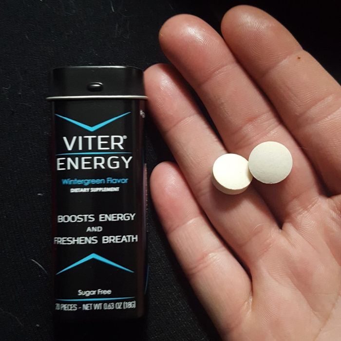 A reviewer's hand holding two round mints beside a Viter Energy tin. The label on the tin reads: