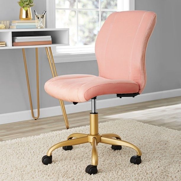 A pink desk chair with gold legs sitting on a carpet.