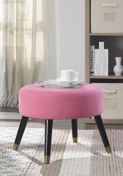 Pink ottoman with black legs, topped with magazines and a white coffee cup.