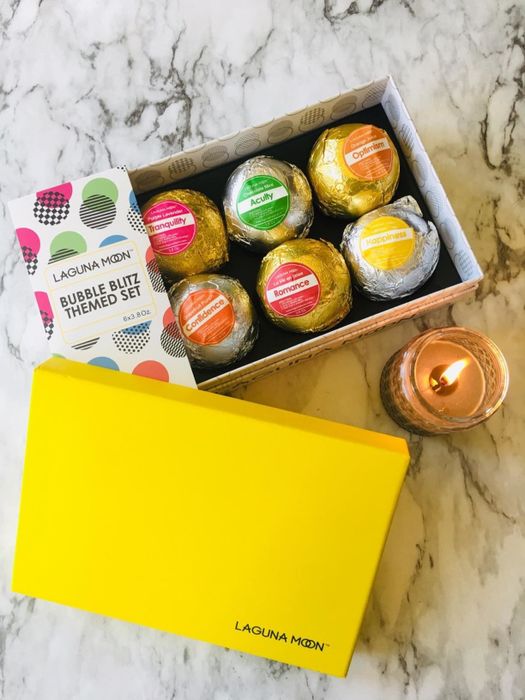 A reviewer image shows the box of bath bombs placed next to a lit candle.
