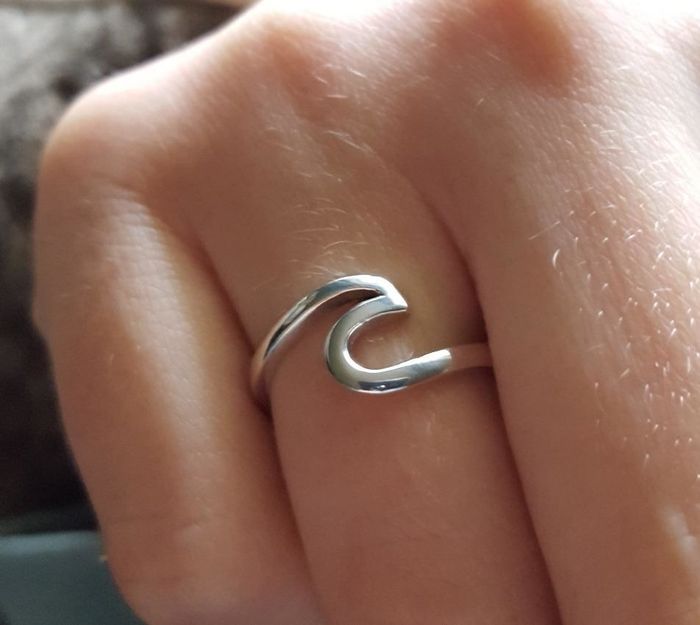 A reviewer showing off the silver ring, designed as the outline of a wave