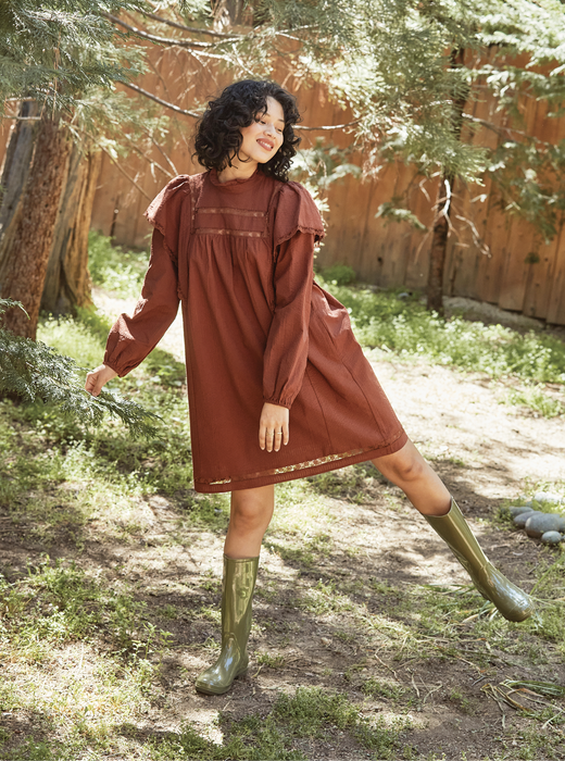 A model showcasing the brown dress while standing in a lawn.