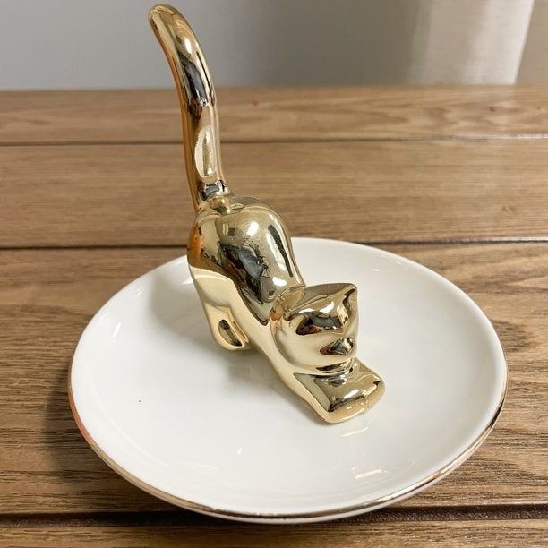 A white dish ring holder featuring a gold cat at its center
