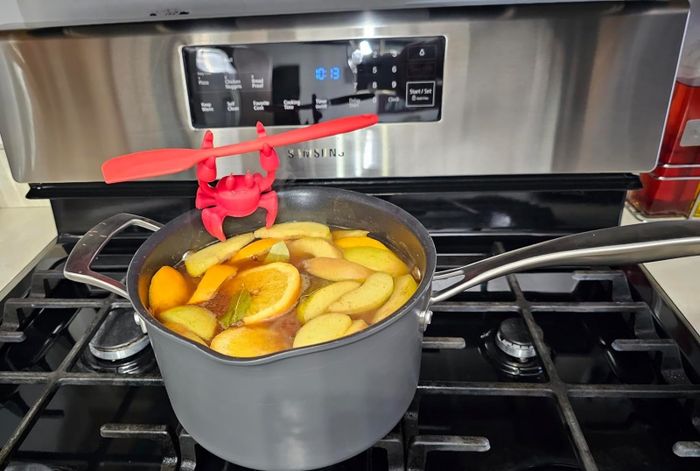 The crab-shaped pot clip attached to the edge of a reviewer's pot, holding a spatula in place