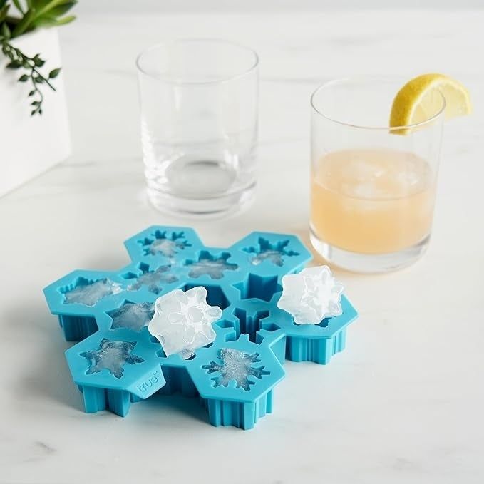 A snowflake-shaped ice mold with ice cubes next to two glasses of drinks, one garnished with a lemon slice