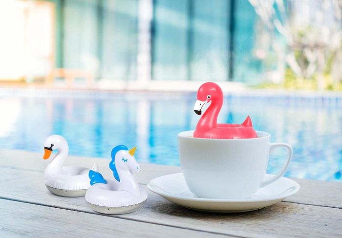 A flamingo-shaped tea infuser resting in a mug, alongside swan and unicorn diffusers