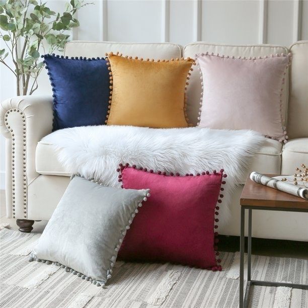 Velvet throw pillows on a couch, from left to right: navy pillow, yellow pillow, light pink pillow, gray pillow on the floor to the bottom left next to a red pillow