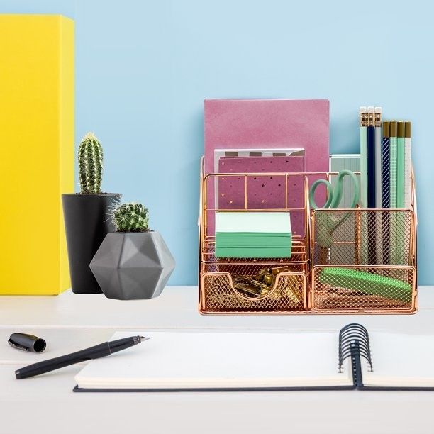 A rose gold desk organizer placed on a desk, surrounded by various office supplies.