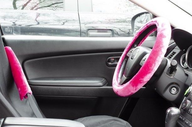 A pink velvet steering wheel cover and matching seatbelt pads installed in a car with black interior.