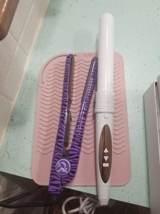 A reviewer demonstrating a straightener and curling iron placed on the textured silicone mat