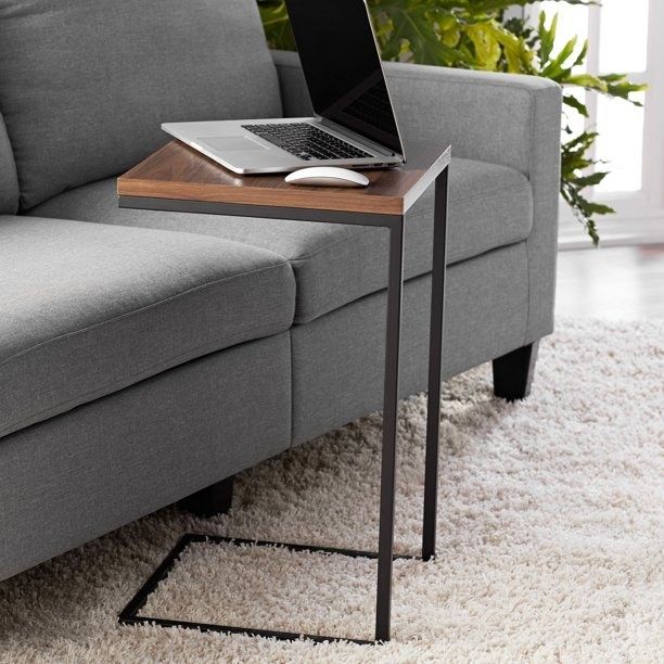 A dark brown c-shaped side table positioned next to a beige chair.