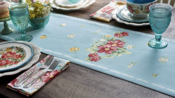 A white and blue table runner with a colorful floral design in the center.