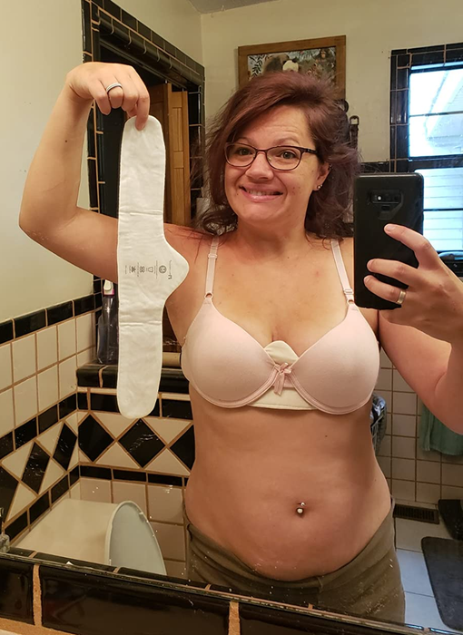 a reviewer smiling while wearing a bra with one of the liners in place and holding another liner in their hand