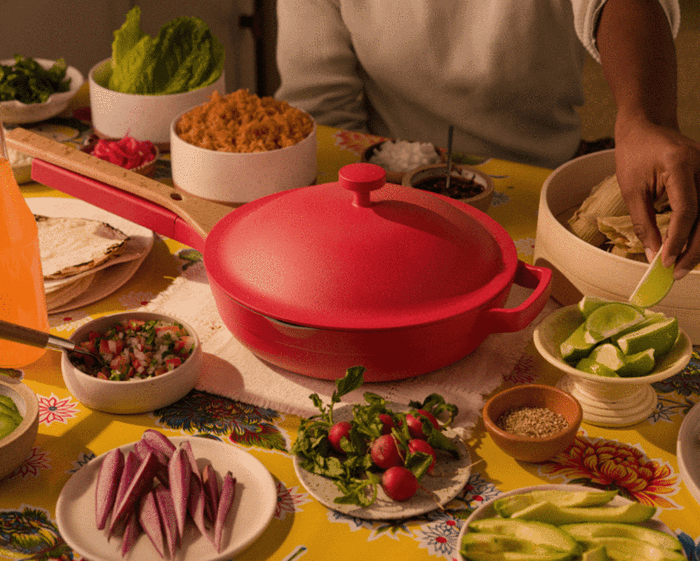 The vibrant Always Pan from Our Place is placed on a table full of plated food.