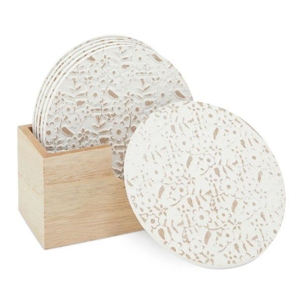 A white ceramic coaster with a floral design placed in front of a wooden container filled with more coasters.