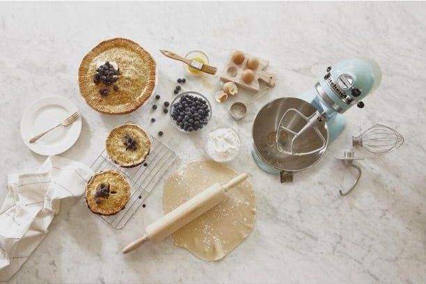 A light blue KitchenAid stand mixer placed on a countertop, surrounded by freshly baked goods and baking tools.