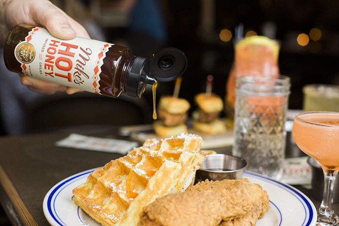 A model drizzles Mike's Hot Honey over a plate of crispy chicken and fluffy waffles.
