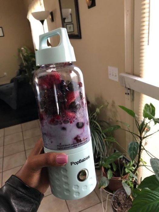 A reviewer holds their personal blender, packed with fresh berries.