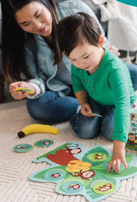 A mother and child are engaged in a lively matching game with a monkey theme. The child excitedly points at a card while the mother looks on with a smile. A toy banana adds a fun touch to the scene.