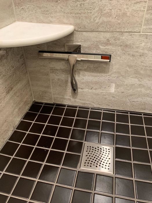 A reviewer’s photo of a sleek silver squeegee hanging in a modern grey and black shower.