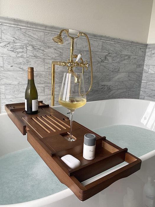 A photo from a reviewer featuring a dark wooden tray holding wine and toiletries, elegantly placed across a spacious white bathtub.