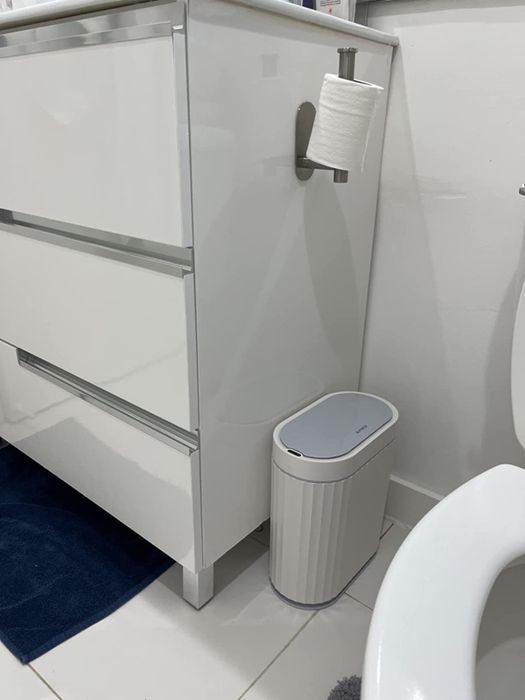 a photo from a reviewer showcasing a compact white trash can neatly placed in a white-themed bathroom