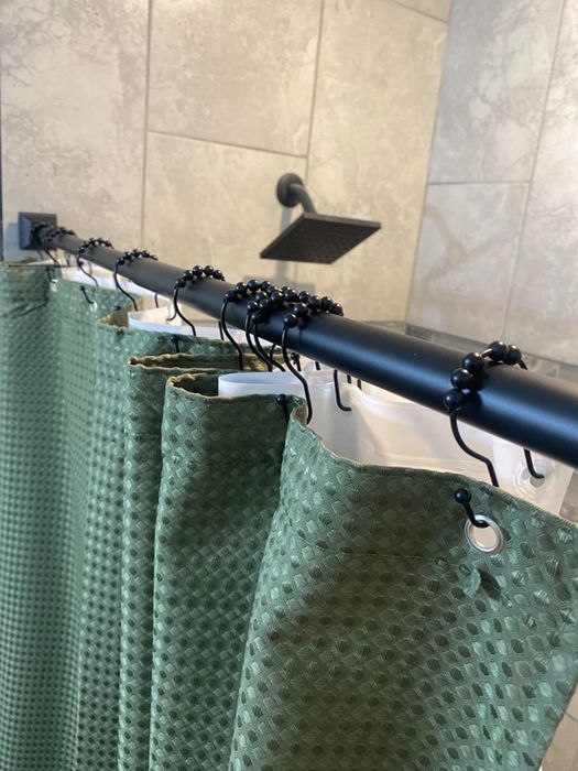 A reviewer's image showcasing dark dual hooks supporting a green shower curtain and a white liner.