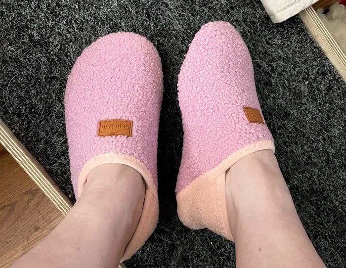 Two feet adorned with plush, textured slippers resting on a carpet. The slippers include a small leather detail