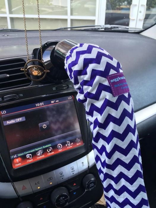 A car's interior with a purple and white patterned cover on the gear shift, audio display screen, and various controls.