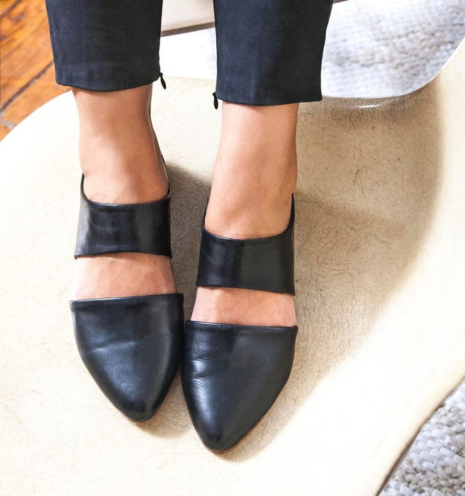 A model showcasing the pointed-toe, open-back flats with a stylish cutout design over the top of the foot