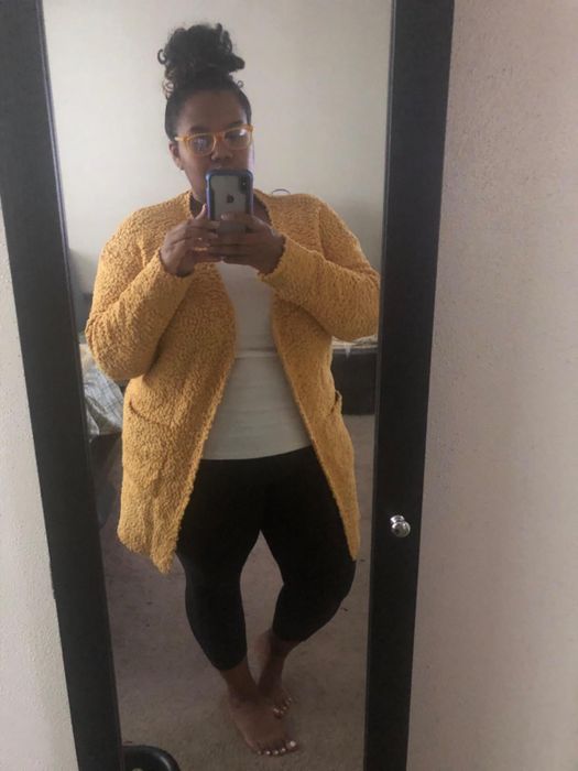 A reviewer capturing a mirror selfie, showcasing the cardigan in a sunny yellow shade