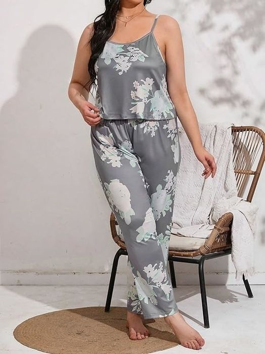 A person posing in a floral-patterned pajama set, standing next to a wicker chair in a minimalist room