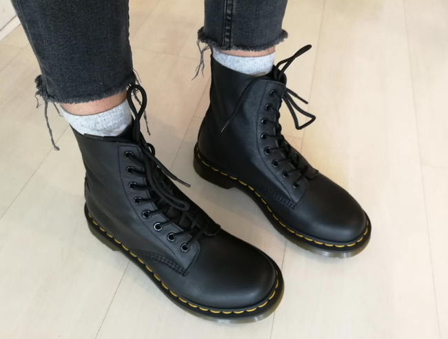 A reviewer showcasing the lace-up boots, featuring distinctive yellow stitching along the sole.