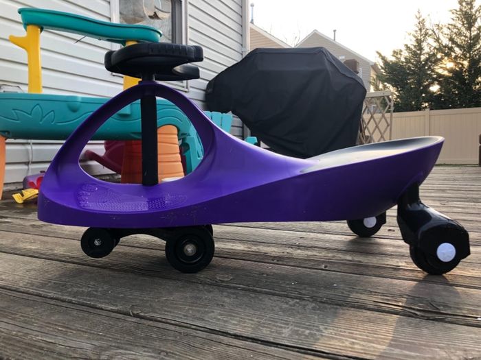 A child's purple ride-on toy car on a wooden deck, with outdoor play equipment in the background