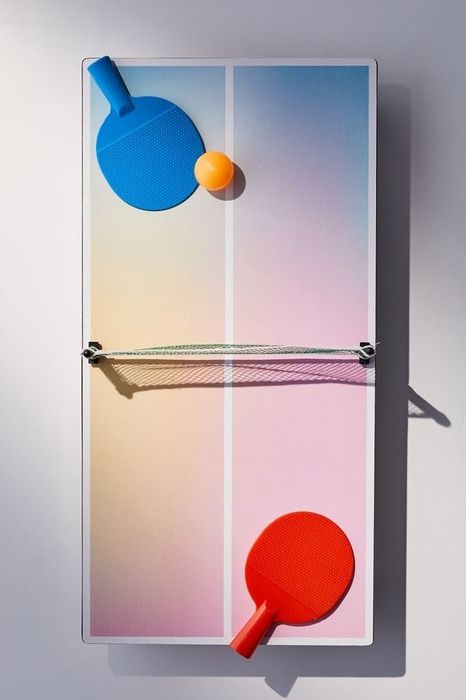 This petite table boasts a pink and blue gradient design, accompanied by red and blue paddles and an orange ball, making it both stylish and functional for indoor games.
