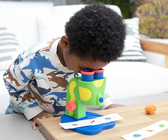 A child peering through a toy microscope at a table