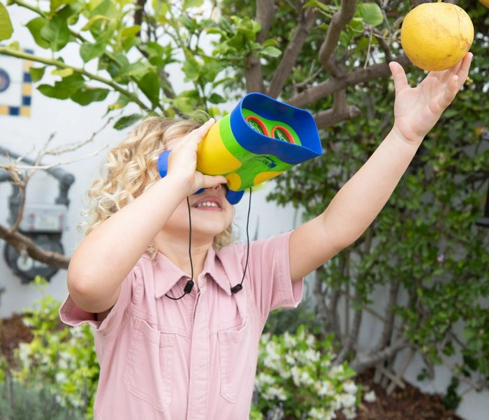 A child enjoying binoculars, reaching out for fruit, while engaging in STEM-focused learning