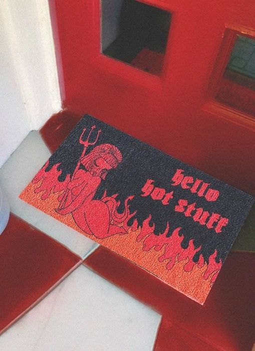 a black doormat featuring flames and a devil, with the playful message 'hello hot stuff'