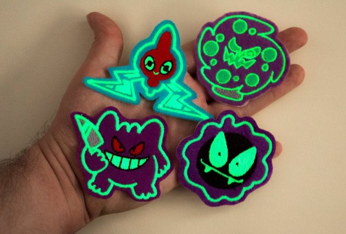 a hand holding patches featuring designs of Ghastly, Gengar, Spiritomb, and Rotom