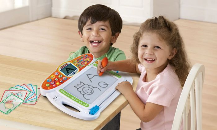 Two children joyfully engaging with an interactive drawing tablet at a table, with a variety of picture cards spread out before them