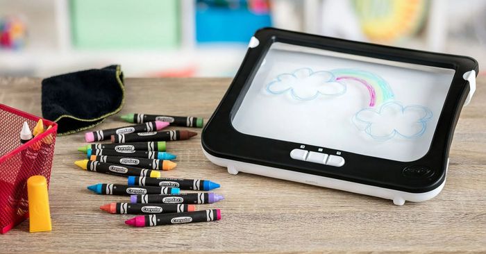 A child’s drawing board with rainbow and cloud designs sits on a table, surrounded by colorful crayons, a red mesh pen holder, and an eraser