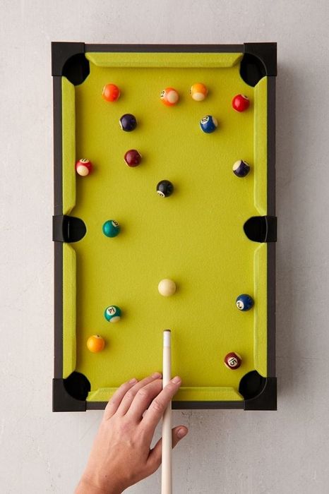 The model demonstrates using a small cue on a lime-green pool table, showcasing the table's vibrant design and compact size.