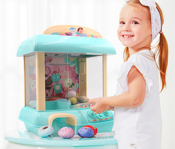 A child standing beside a compact plastic claw machine.
